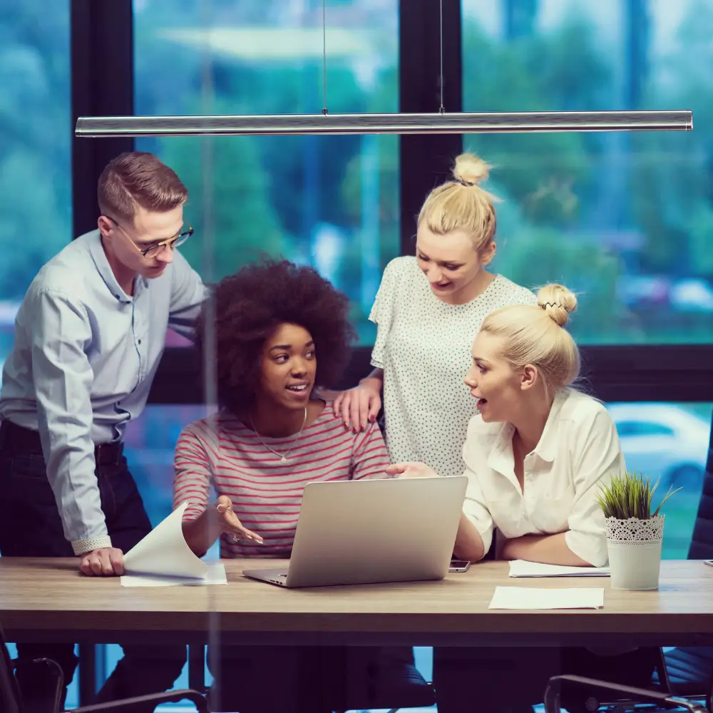 group of people in an office gathered around a laptop